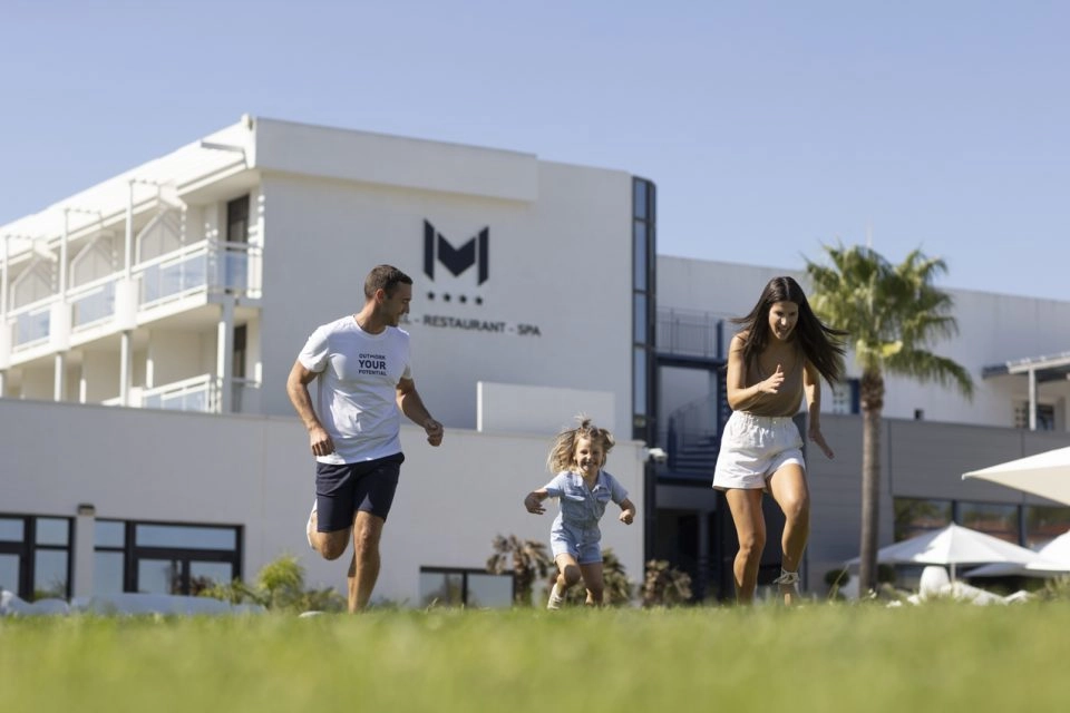 famille court dans l'herbe devant hotel avec piscine mouratoglou