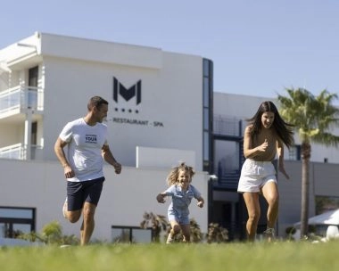 famille court dans l'herbe devant hotel avec piscine mouratoglou