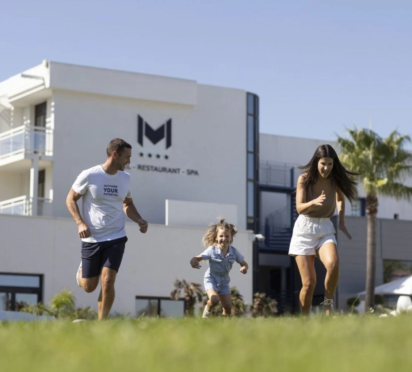 famille court dans l'herbe devant hotel avec piscine mouratoglou